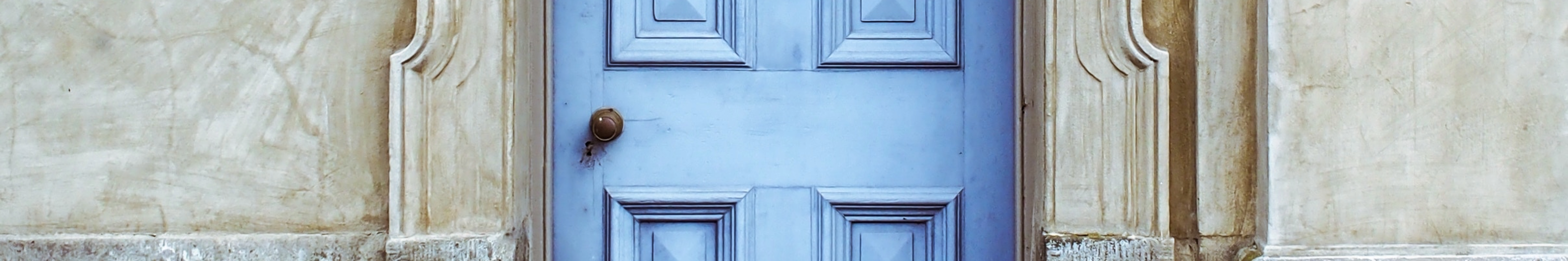 Panoramic crop of a light blue paneled wooden door with a brass knob, set in a weathered stone wall.